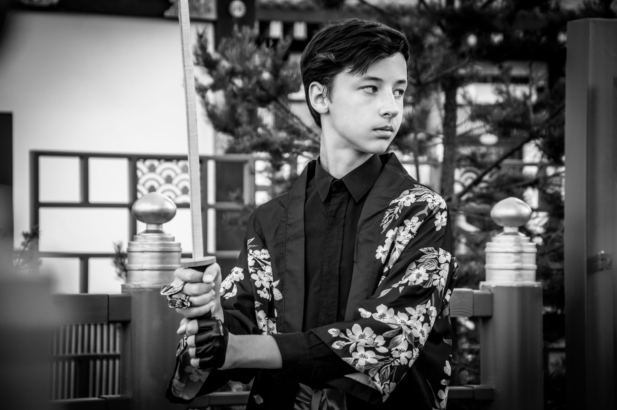 Black and white portrait of a teenager in a kimono holding a katana sword in a Japanese-styled setti
