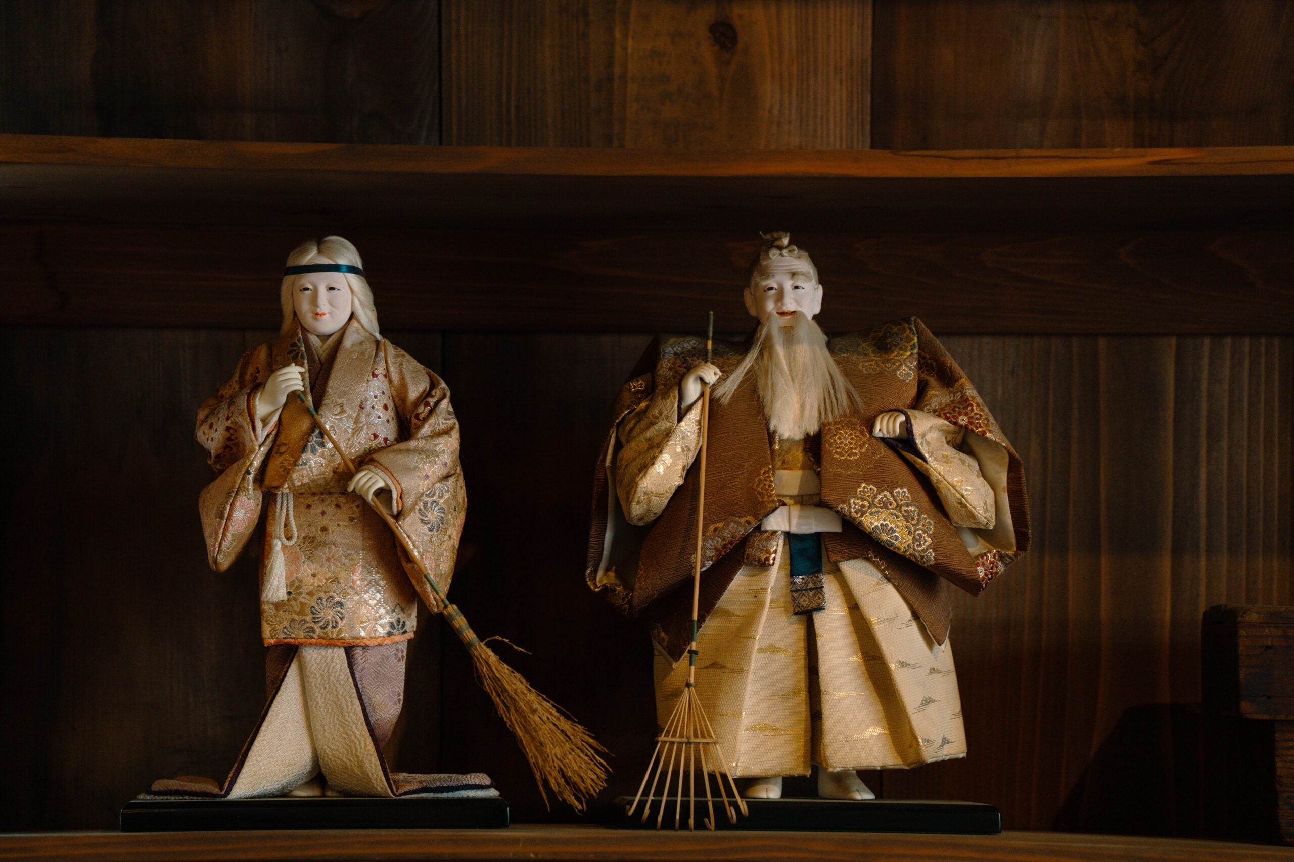 Two ornate Japanese dolls in traditional attire displayed on a wooden shelf.