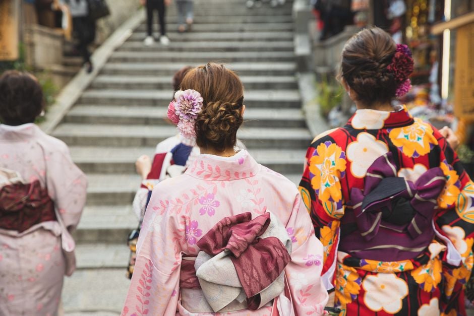 Back view of unrecognizable Asian women in kimonos walking on street against stone staircase in down